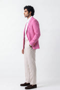 A man standing in profile wearing a bright pink hemp blazer over a white shirt and light beige trousers, paired with dark brown loafers, against a plain white studio background.