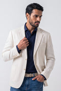 A man wearing a light beige hemp blazer over a navy blue shirt and blue jeans, posing against a light gray studio background.