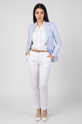 A woman modeling a light blue linen blazer, white shirt, white trousers, and white heels against a light gray studio background.