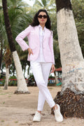Woman in light pink blazer and white pants standing under a palm tree.