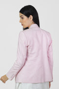 Woman wearing a light pink linenvblazer with a subtle pattern on a white background.