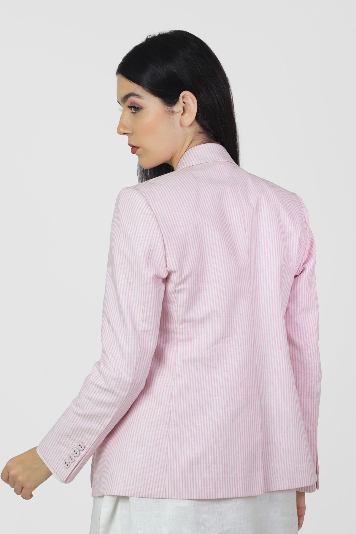 Woman wearing a light pink linenvblazer with a subtle pattern on a white background.