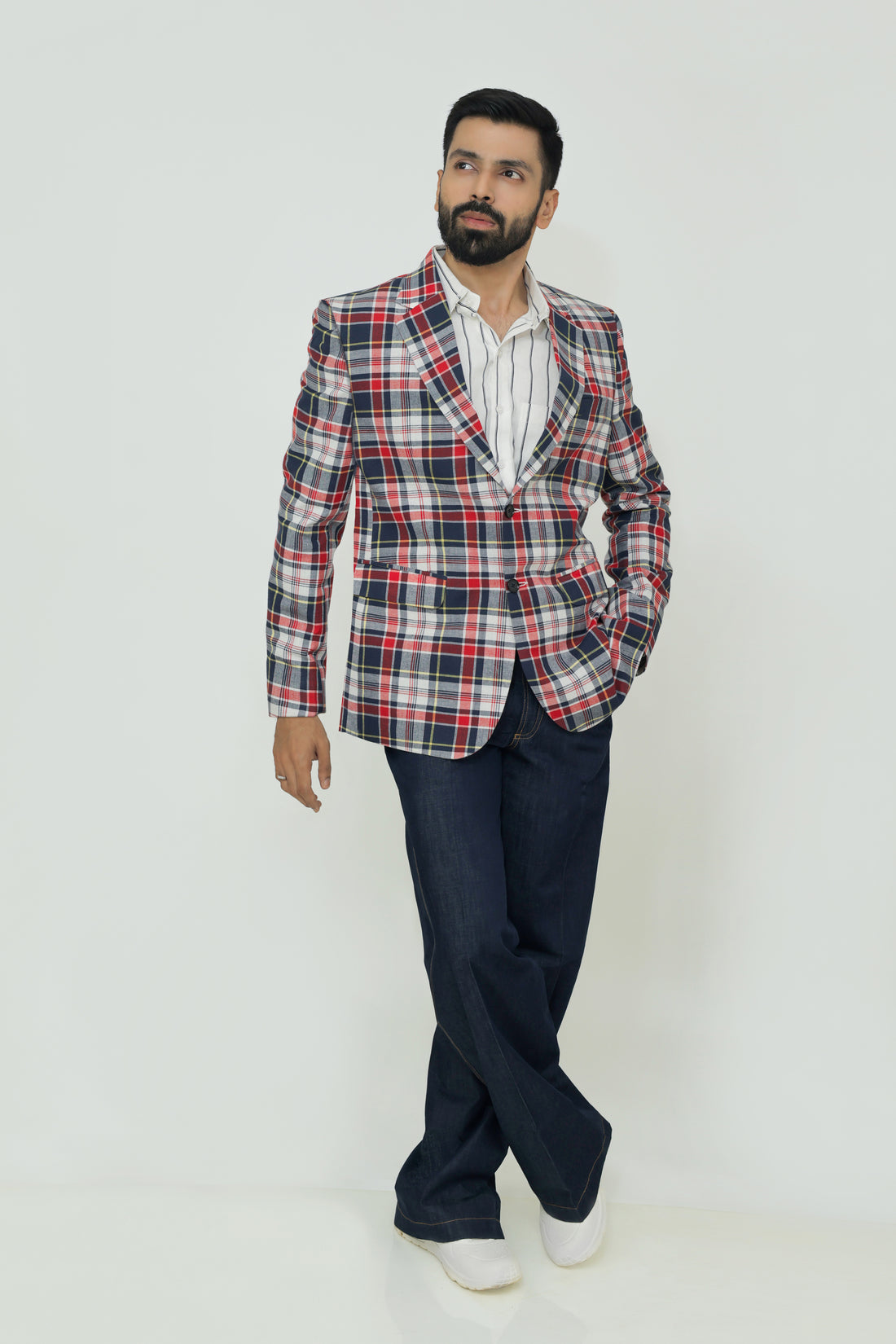 A man wearing a red, blue, and white checkered linen blazer with notch lapel, two-button front, flap pockets, and a chest pocket. He is also wearing a white shirt and dark trousers.