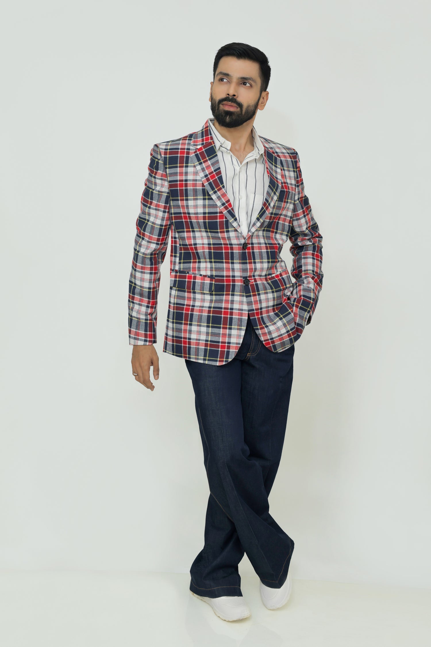 A man wearing a red, blue, and white checkered linen blazer with notch lapel, two-button front, flap pockets, and a chest pocket. He is also wearing a white shirt and dark trousers.