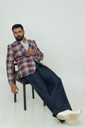 A man wearing a red, blue, and white checkered linen blazer with notch lapel, two-button front, flap pockets, and a chest pocket. He is also wearing a white shirt and dark trousers.