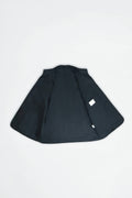 A black inside of jacket or cape-style outerwear piece laid flat on a light gray background, featuring a small white rectangular tag near the lower right side.