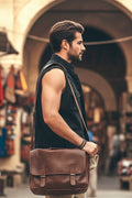 Man holding a brown leather bag in an outdoor market setting
