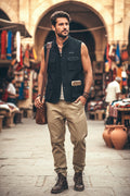 Man in a sleeveless black vest and beige pants standing in an outdoor market setting.