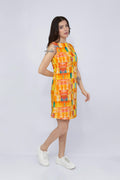 A woman modeling a sleeveless, knee-length hemp dress with a vibrant abstract geometric pattern in orange, yellow, and blue, paired with white sneakers, against a light gray studio background.