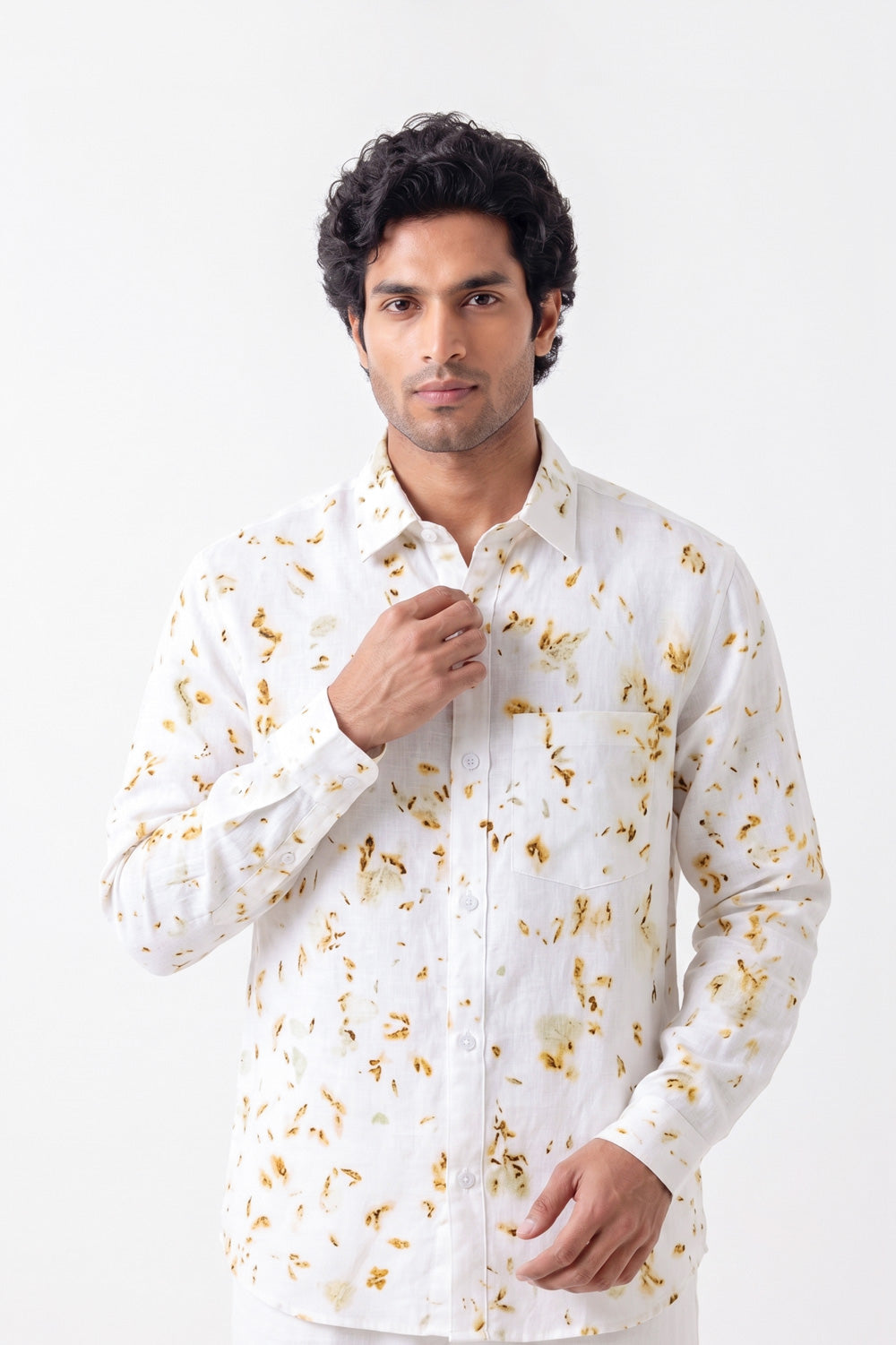 A man wearing a white long-sleeve button-up shirt with a gold abstract floral pattern, posing against a plain white background.