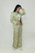 A woman modeling a floral silk blazer with a notch lapel and two-button closure. The blazer is in a light multicolor pattern.