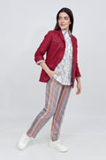A woman modeling a burgundy linen jacket over a white patterned shirt, paired with colorful vertically striped trousers and white sneakers, against a light gray studio background.