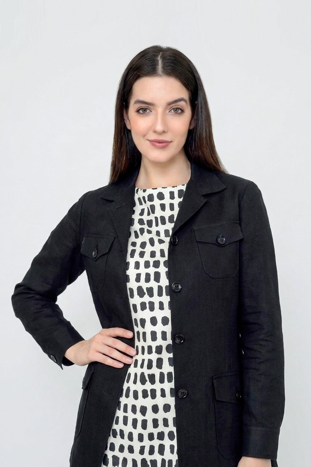 A woman modeling a black button-front linen jacket over a black-and-white patterned dress, photographed against a plain light gray studio background.