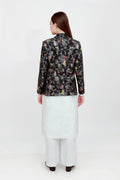A woman modeling a silk blazer with a floral pattern, wearing a white shirt and pants.