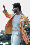 Man wearing a colorful checkered jacket over a white shirt and pants, standing on a rocky beach.
