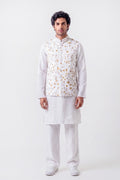 A man modeling a white traditional Indian outfit consisting of a kurta, trousers, and a white embroidered vest with gold and orange floral patterns, shot against a plain white studio background.