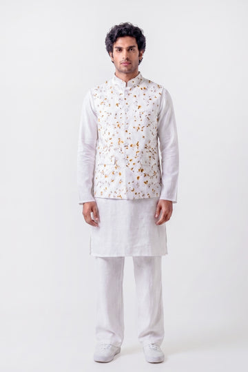 A man modeling a white traditional Indian outfit consisting of a kurta, trousers, and a white embroidered vest with gold and orange floral patterns, shot against a plain white studio background.