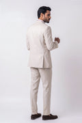 A man shown from the back wearing a light beige textured linen suit with a white shirt and dark brown loafers, standing against a plain white studio background.