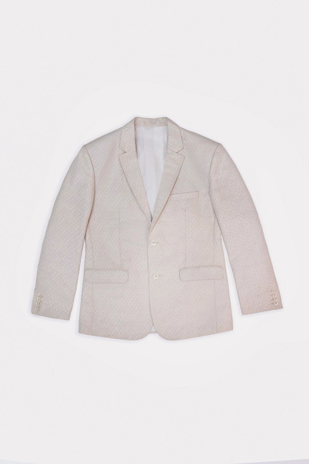 A man modeling a light beige linen suit with a white dress shirt and dark brown loafers, standing against a plain white studio background.