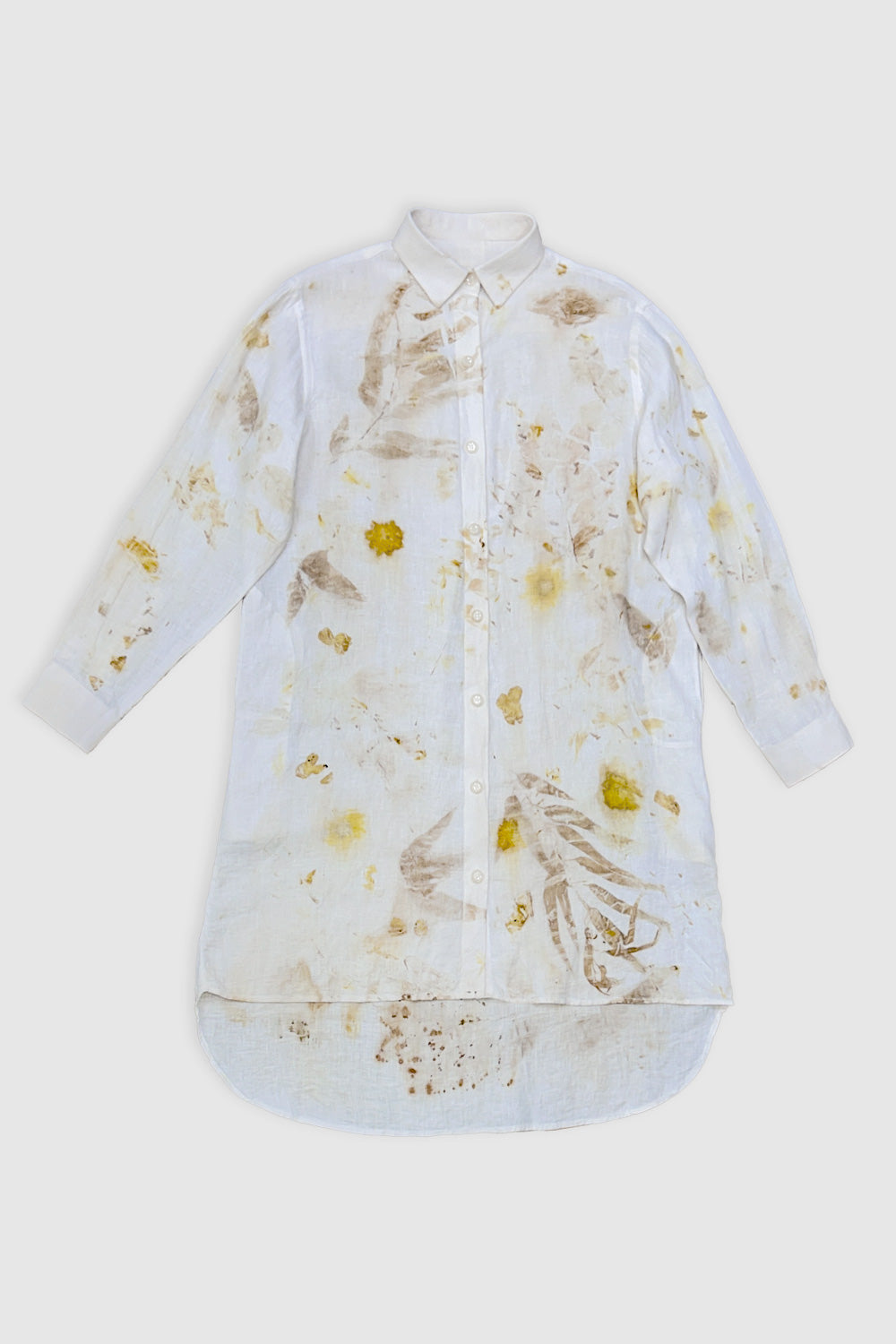 A woman modeling a white long-sleeve button-up shirt dress with a yellow and beige botanical print, standing against a plain white studio background.