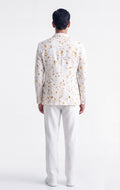 A man viewed from the back wearing a white long-sleeve blazer with a delicate gold floral pattern and white trousers, set against a plain white studio background.