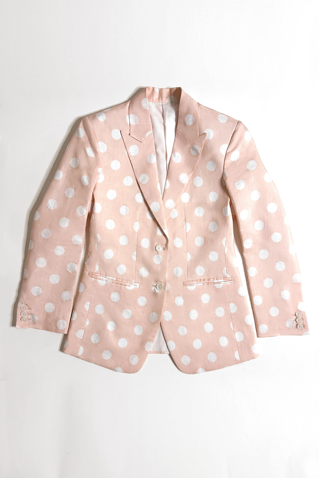 A woman model wearing a peach hemp blazer with a peak lapel, two buttons, and flap pockets, paired with white trousers.
