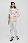 A woman model wearing a peach hemp blazer with a peak lapel, two buttons, and flap pockets, paired with white trousers.