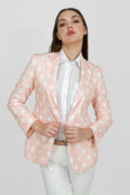 A woman model wearing a peach hemp blazer with a peak lapel, two buttons, and flap pockets, paired with white trousers.