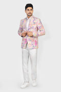 Man wearing a colorful floral blazer with white pants on a white background