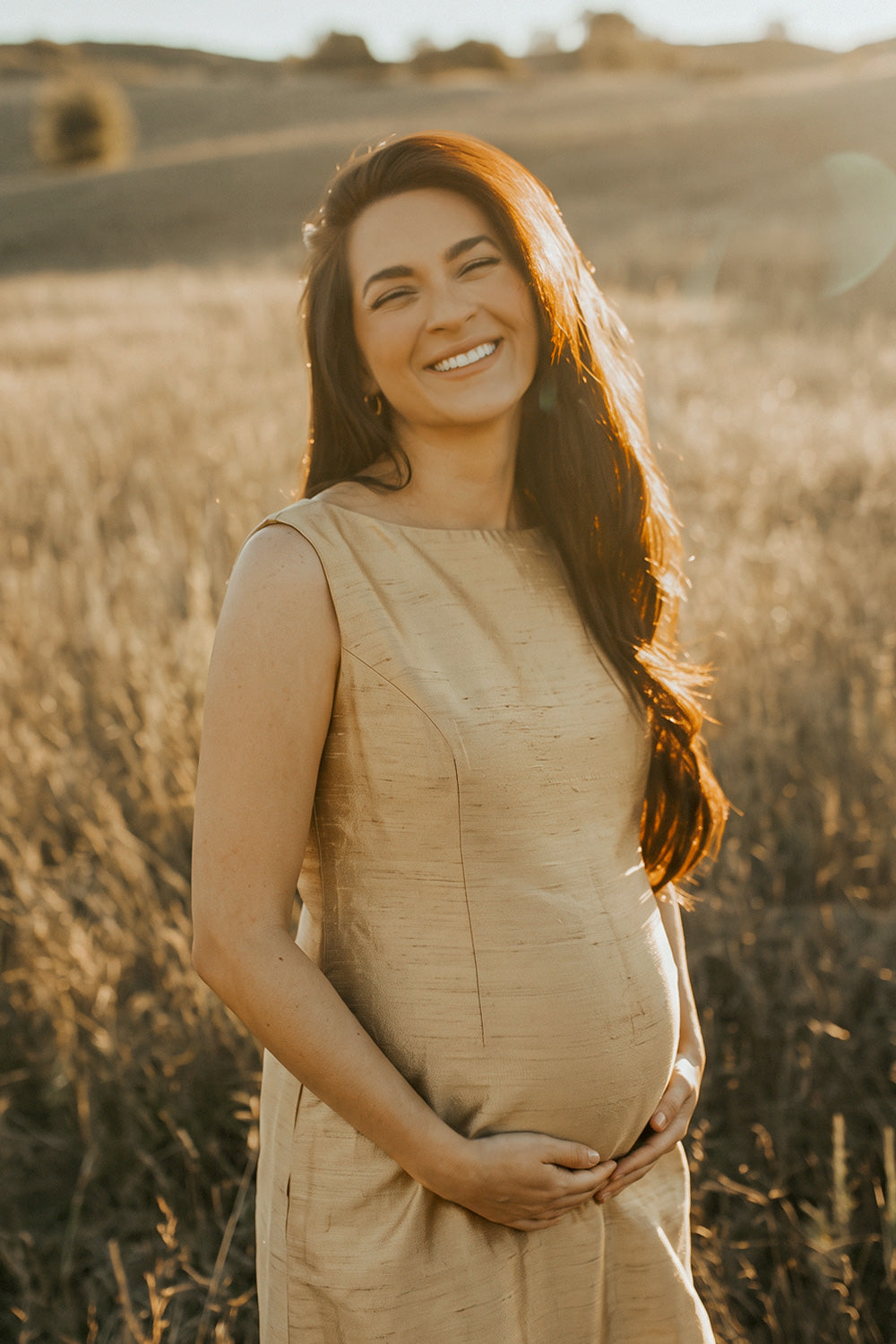 Pregnant woman wearing a natural silk maternity dress in a sunlit field, showcasing elegant sustainable maternity fashion.