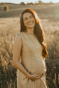 Pregnant woman wearing a natural silk maternity dress in a sunlit field, showcasing elegant sustainable maternity fashion.