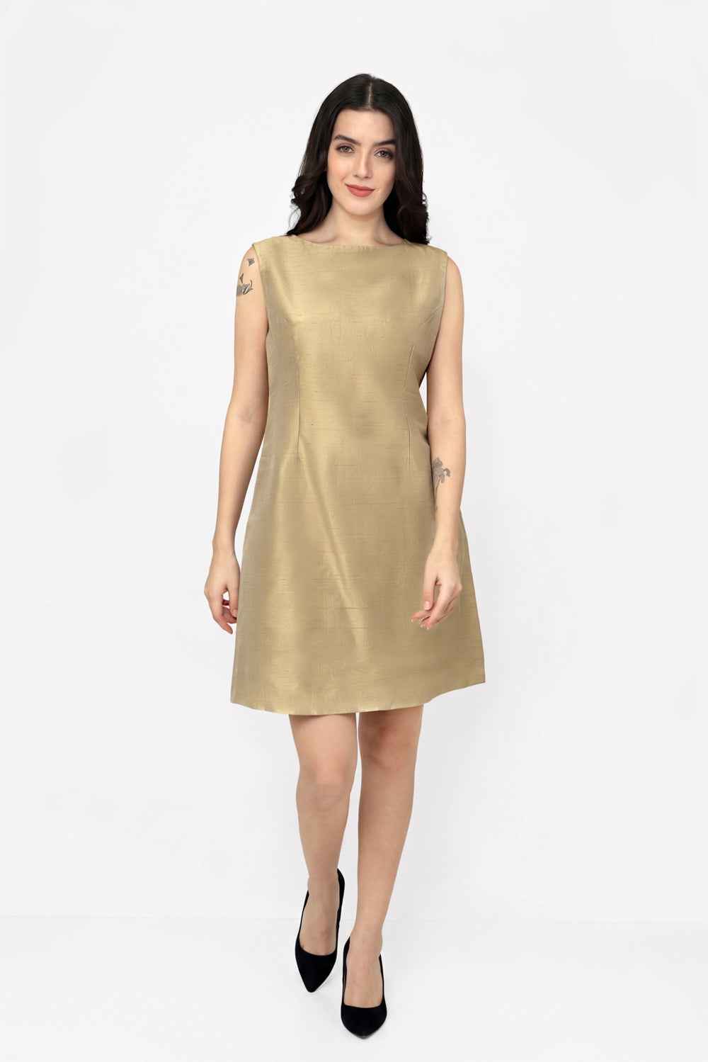 A woman modeling a sleeveless, knee-length A-line silk dress in a metallic gold color, paired with black pointed-toe heels, against a plain white studio background.
