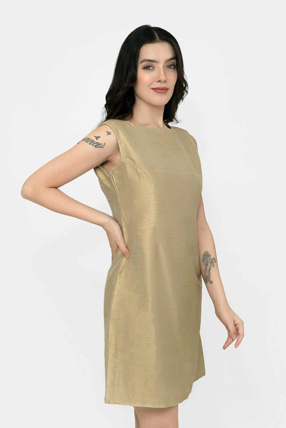 A woman modeling a sleeveless, knee-length A-line silk dress in a metallic gold color, paired with black pointed-toe heels, against a plain white studio background.