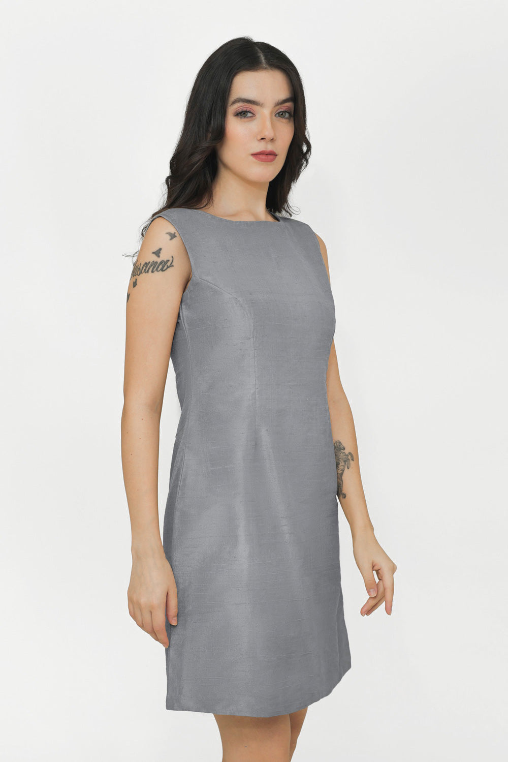 A woman modeling a sleeveless, knee-length gray silk dress against a plain white studio background.