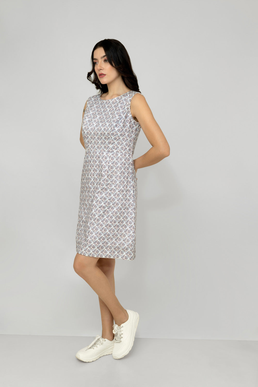 A woman models a mid-length sleeveless linen dress with a geometric pattern, featuring a boat neck and rear zip opening.