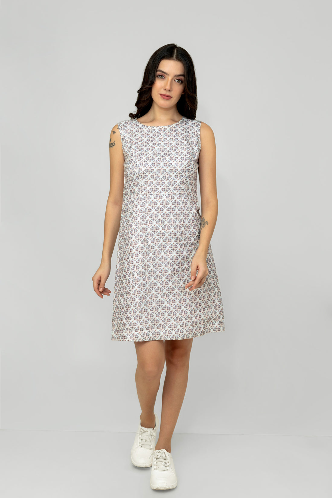A woman models a mid-length sleeveless linen dress with a geometric pattern, featuring a boat neck and rear zip opening.
