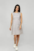 A woman models a mid-length sleeveless linen dress with a geometric pattern, featuring a boat neck and rear zip opening.