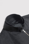 Close-up of a black linen jacket with a ribbed knit stand collar, snap button, and a partial silver zipper on a light gray background.