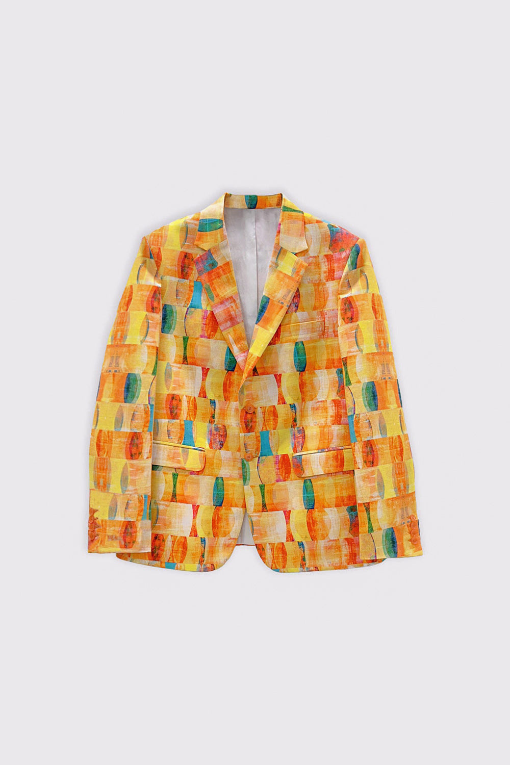 A man modeling a vibrant yellow, orange, and green abstract-patterned hemp blazer over a white button-down shirt, paired with blue jeans and white sneakers, against a plain light background.