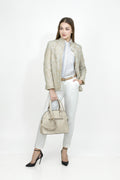 Woman in a stylish outfit with a beige blazer, white pants, and a beige handbag on a white background