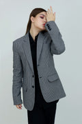 A person wearing a single-breasted, gray, checkered unisex cotton jacket with a notch lapel and functional sleeves, paired with a black outfit.
