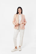 Woman wearing a light pink blazer over a white shirt and pants on a white background
