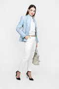Woman wearing a light blue blazer, white top, and pants with a handbag on a white background