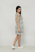 A woman wearing a sleeveless, knee-length black and white hemp dress with a boat neckline, standing before white background