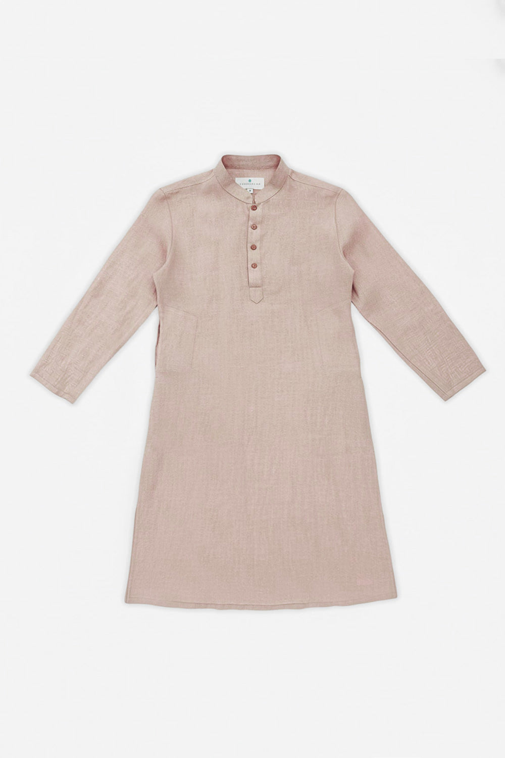 A man modeling a light beige linen kurta with a buttoned mandarin collar, paired with white trousers and white sneakers, standing against a plain white studio background.