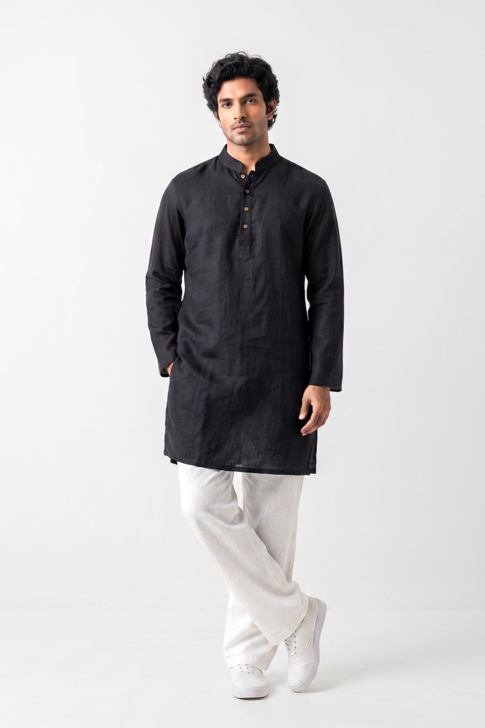 A man modeling a black long-sleeve Linen kurta with a mandarin collar and three-quarter buttons, paired with white trousers and white sneakers, against a plain white studio background.