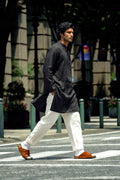 A man walking across a city crosswalk wearing a black long-sleeve linenkurta, white trousers, and brown leather sandals.