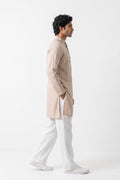 A man in profile wearing a light beige linen kurta and white trousers, standing against a plain white studio background.
