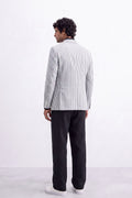 A man shown from the back wearing a light gray and white vertically striped linen blazer, black trousers, and white sneakers, standing against a plain white studio background.