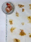 Onions in a glass bowl beside hemp-cotton fabric eco-printed with onion skins